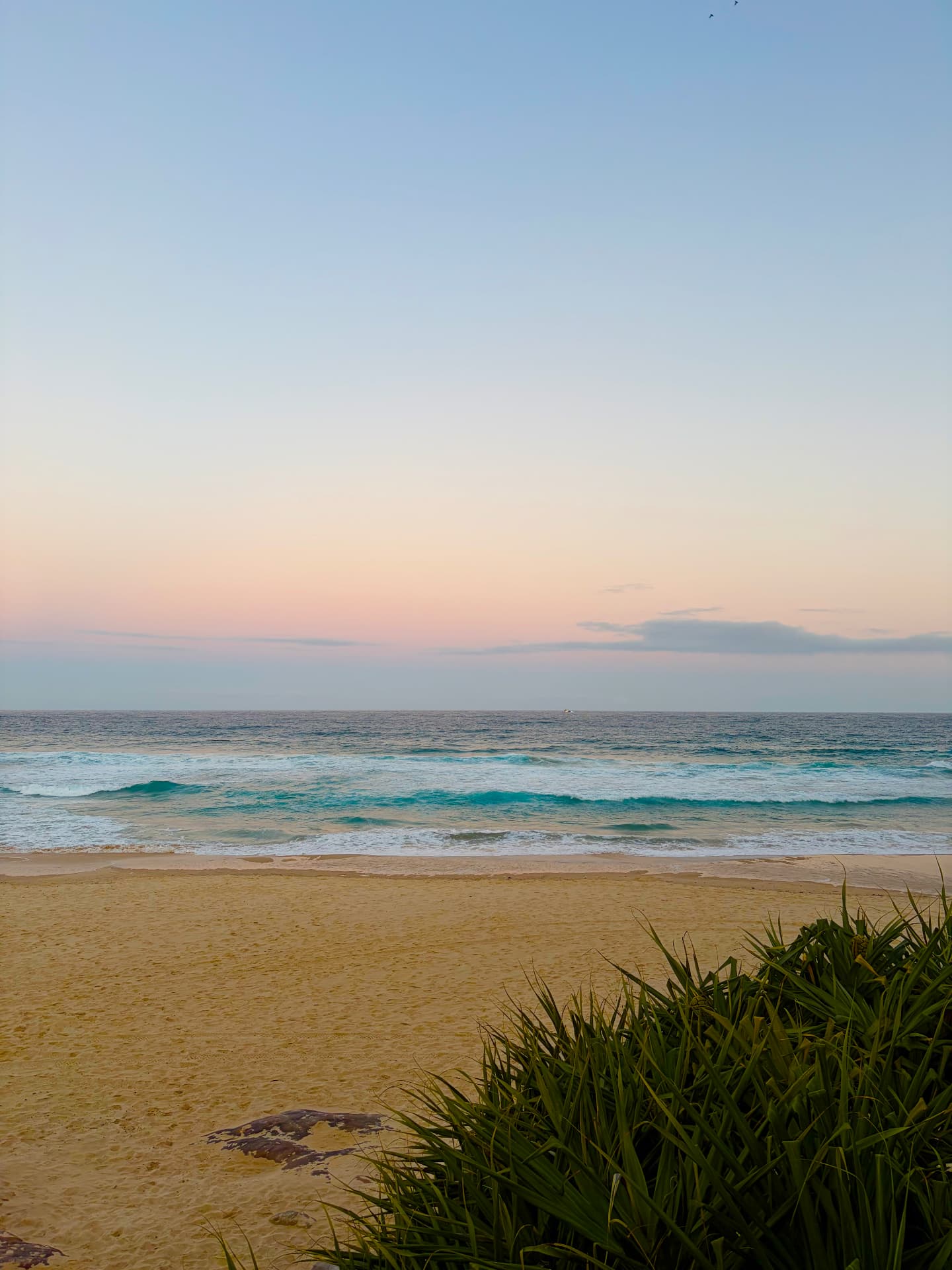 A beach at dusk under a soft pastel sky
